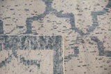 Corner of a distressed rug showing blue hand-knotted pile over the ivory cotton foundation.