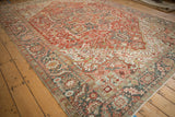 Distressed Heriz carpet corner with abrashed cherry red field, geometric motifs, and serrated leaf palmette border.