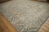 Vintage distressed Persian Heriz carpet showing geometric patterns in faded beige, pale blue, and charcoal tones.
