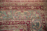 Corner of a distressed antique Yezd rug with floral borders in raspberry magenta and jade green.