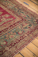 Angled close-up on the intricate floral borders and raspberry field of a distressed Yezd carpet.
