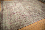 Angled view of an antique Kerman carpet showing its time-softened raspberry and platinum floral pattern.