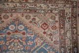Corner detail of an antique Malayer rug featuring worn texture with sky blue, beige, and copper motifs.