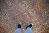 Distressed vintage Bakhtiari garden motif carpet in ruby red, sky blue, and ivory tones, with human feet.