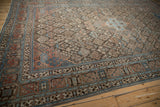 Distressed Persian Joshegan carpet corner, displaying ornate borders and patterned field in blue, red.