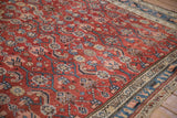 Angled close-up of a vintage Hamadan carpet showing color abrashes in the saturated red Herati field.