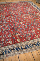Corner view of a vintage Kurdish carpet showing the blue main border and saturated red Herati field.