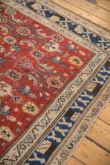 Angled close-up of a vintage Kurdish carpet's thick pile, cherry red field, and blue floral border.