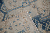 Distressed vintage Bakhtiari carpet corner; ivory and blue pattern, hand-knotted pile, and bound edge.