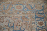 Corner of a distressed Heriz rug featuring serrated leaf and floral borders in sky blue and sand.
