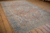 A distressed Persian Heriz rug from an angle, with a faded sandalwood field and bold blue details.