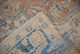 A vintage Heriz carpet with corner folded back to show the hand-knotted foundation and distressed pile.