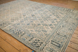 Distressed texture of a vintage Joshegan carpet showing dusty teal floral sprays and a wide arabesque border.