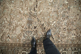 Black boots on a distressed vintage Heriz rug, showing worn beige and blue geometric motifs.