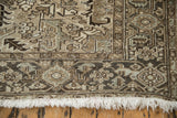 Distressed vintage Heriz carpet corner with muted geometric pattern, visible wear, and cream fringe.