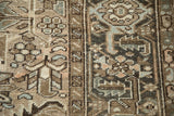 Worn pile and geometric patterns on a distressed Heriz rug in earthy tones.