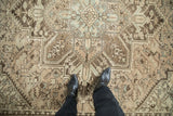 Person's view of the even wear and central medallion of a vintage distressed Mehrivan carpet.