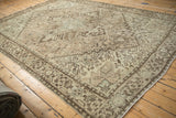 Angled view of a distressed Mehrivan carpet's geometric design in soft sand, ivory, and pale slate tones.