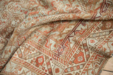 The worn, hand-knotted texture of a distressed Shiraz rug with geometric patterns in rust and dusty blue.