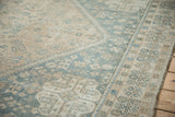 Distressed corner of a vintage Qashqai carpet with a dusty blue border and sand-colored field.