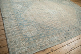 Worn pile and visible knot heads on the corner of a distressed Qashqai rug with pale blue and sand patterns.
