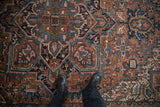 Intricate geometric blossoms and vinery on vintage Heriz carpet in brick red, navy, and pink.