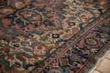 Vintage Heriz rug detail with brick red, navy blue geometric blossoms, serrated leaves, and fringe.