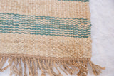 Emmy Collection natural jute rug with coarse texture, teal stripes, and fringe.