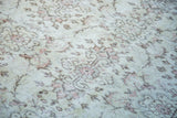 Distressed ivory Oushak rug pile with faded pink and brown allover floral motifs.