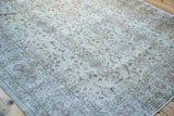 Distressed vintage Oushak rug corner, showing faded ivory pile, soft pink floral motifs, and muted border.