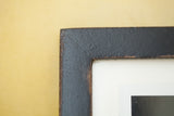 Corner detail of a black handmade frame with a textured, vintage-style finish.