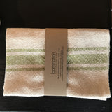 Loomination handwoven napkin with lime green stripes, cream texture, and brown paper band.