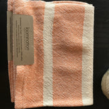 Close-up of Loomination handwoven tangerine orange and white striped towel, showing folded tag.