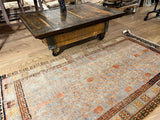 Industrial coffee table cart with dark reclaimed wood top, rustic base, and metal caster wheel.