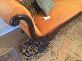 Intricately carved dark wood armrest and tangerine orange velvet upholstery of the Phyfe style sofa.