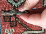 Aged vintage African brass elephant sculpture held between fingers on a colorful patterned rug.