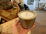 Hand holding a concrete vessel candle with gold triangles, showing the top label.