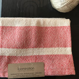Loomination handwoven red and white cotton towel, close-up of textured weave and tag.