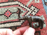 Miniature vintage African brass elephant casting with dark patina and raised trunk.