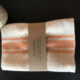 Loomination handwoven napkin set, folded, revealing cream and tangerine stripes and textured weave.