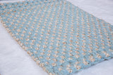 Chunky hand-woven jute rug texture in light blue and natural fibers with braided edge.
