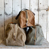 Three Peg and Awl Journey Duffle Bags in tan, olive, and moss green waxed canvas.
