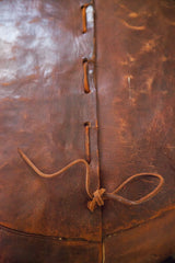 Hand-made antique pouf showing rich, dark orangey leather, knotted lacing, and patina.