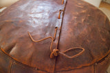 Rich dark orangey leather top of antique pouf, with lacing and natural patina.
