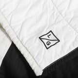 Embroidered Louise Gray LG logo detail on white quilted cotton, next to black fabric.