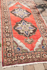 Vintage red Turkish runner with brown medallion, traditional floral border, and fringe.