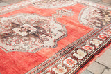 Angled view of vintage Oushak rug showing madder red field, charcoal bronze, and beige motifs.