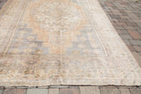 Blanched vintage Oushak carpet end, showing faded ivory, beige, and bronze patterns with soft texture.