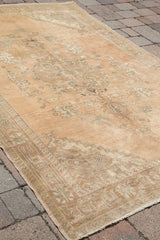 Vintage Oushak rug corner, sun-faded terra cotta field, blanched border, and fringe.