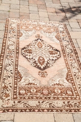 Curvilinear motifs in brown and cream on the peach border of a vintage Oushak rug corner.